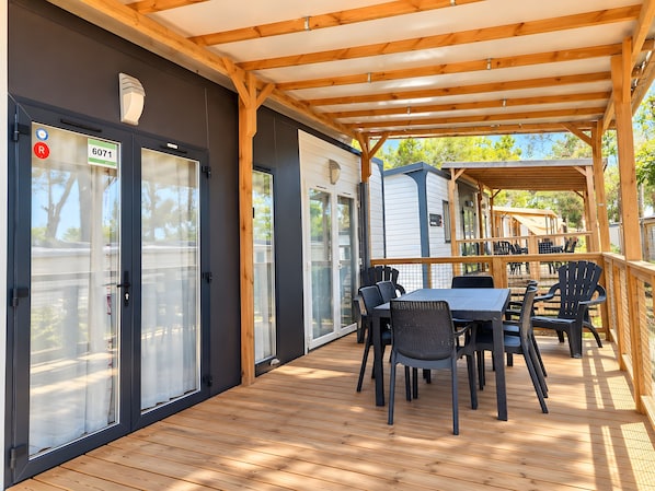An outdoor patio with a wooden deck, a covered seating area, and a view of the surrounding landscape. - Caravan '5-star Family' with Shared Pool, Private Terrace and Air Conditioning (Vendres)