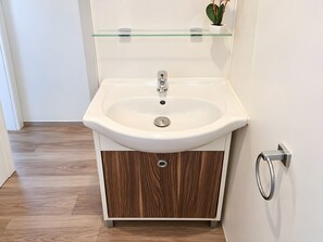 A bathroom with a white sink, wooden cabinet, and a glass shelf above the sink. - Caravan '5-star Family' with Shared Pool, Private Terrace and Air Conditioning (Vendres)