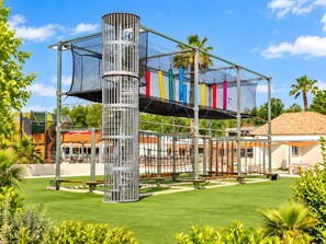 A playground with a climbing structure, a palm tree, and a building in the background.