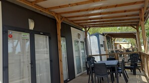 A covered outdoor area with a table and chairs, a covered walkway, and a building with a garage door. - Caravan '5-star Family' with Shared Pool, Private Terrace and Air Conditioning (Vendres)