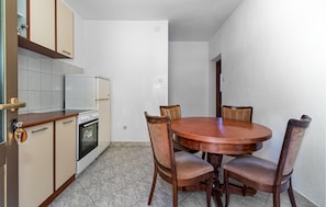 A compact kitchen with a dining area, featuring a round wooden table and four chairs, a built-in oven, and a refrigerator. - Amazing apartment in Crikvenica with WiFi (Crikvenica)