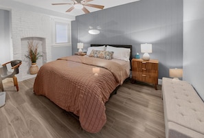 Ein modernes Schlafzimmer mit einem großen Bett, Holz-Nachttischen, einem Deckenventilator und einer kleinen Sitzecke.