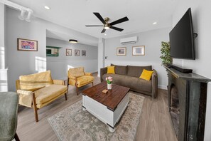 Ein modernes Wohnzimmer mit einer Couch, Sesseln, einem Couchtisch und einem an der Wand befestigten Fernseher.