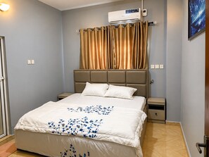 A bedroom with a bed, a nightstand, a wall-mounted air conditioner, and a window with curtains. - Serene 2-Bed-Apt ~ 24hrs Pwr ~ Unlimited Internet (Lagos)