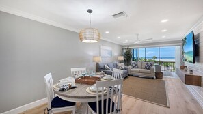 Un salon moderne avec un coin repas, de grandes fenêtres et une vue sur l’océan.