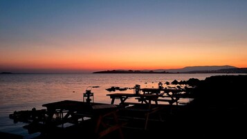 Une vue sur le bord de l’eau, avec un quai et des tables, probablement un restaurant ou un café, au coucher du soleil.