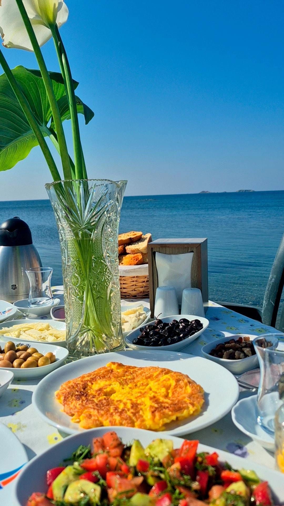 Une table dressée avec différents plats, un vase rempli de fleurs et une vue sur la mer.