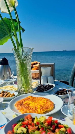A table set with various dishes, a vase with flowers, and a view of the sea. - Bells Beach Hotel (Seferihisar)