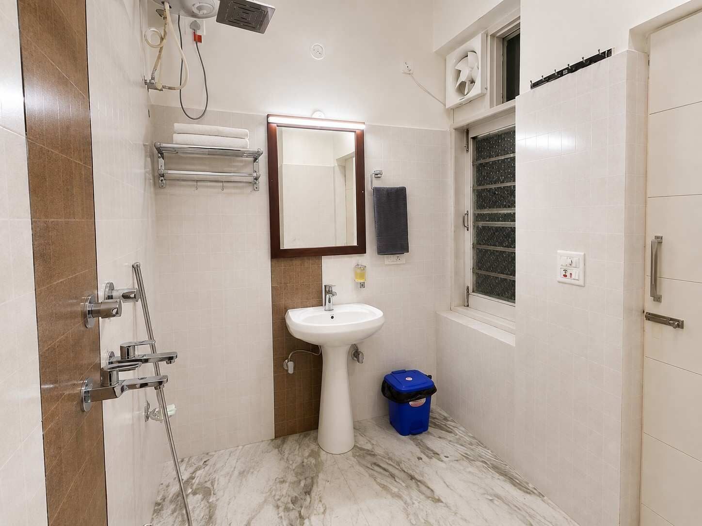 Un baño con lavamanos, espejo, toallero, ducha y ventana.
