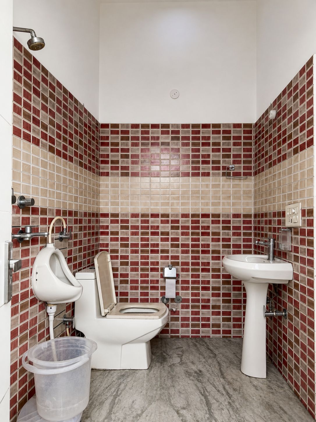 Un baño con inodoro, bidé y lavamanos, con azulejos en rojo y beige.