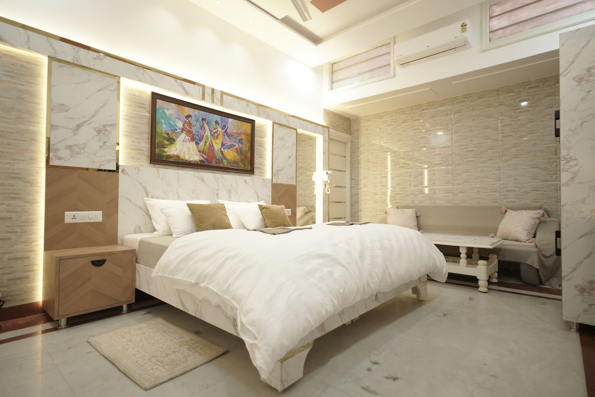Une chambre moderne avec un grand lit, des tables de chevet, une commode, un canapé et un tableau décoratif.
