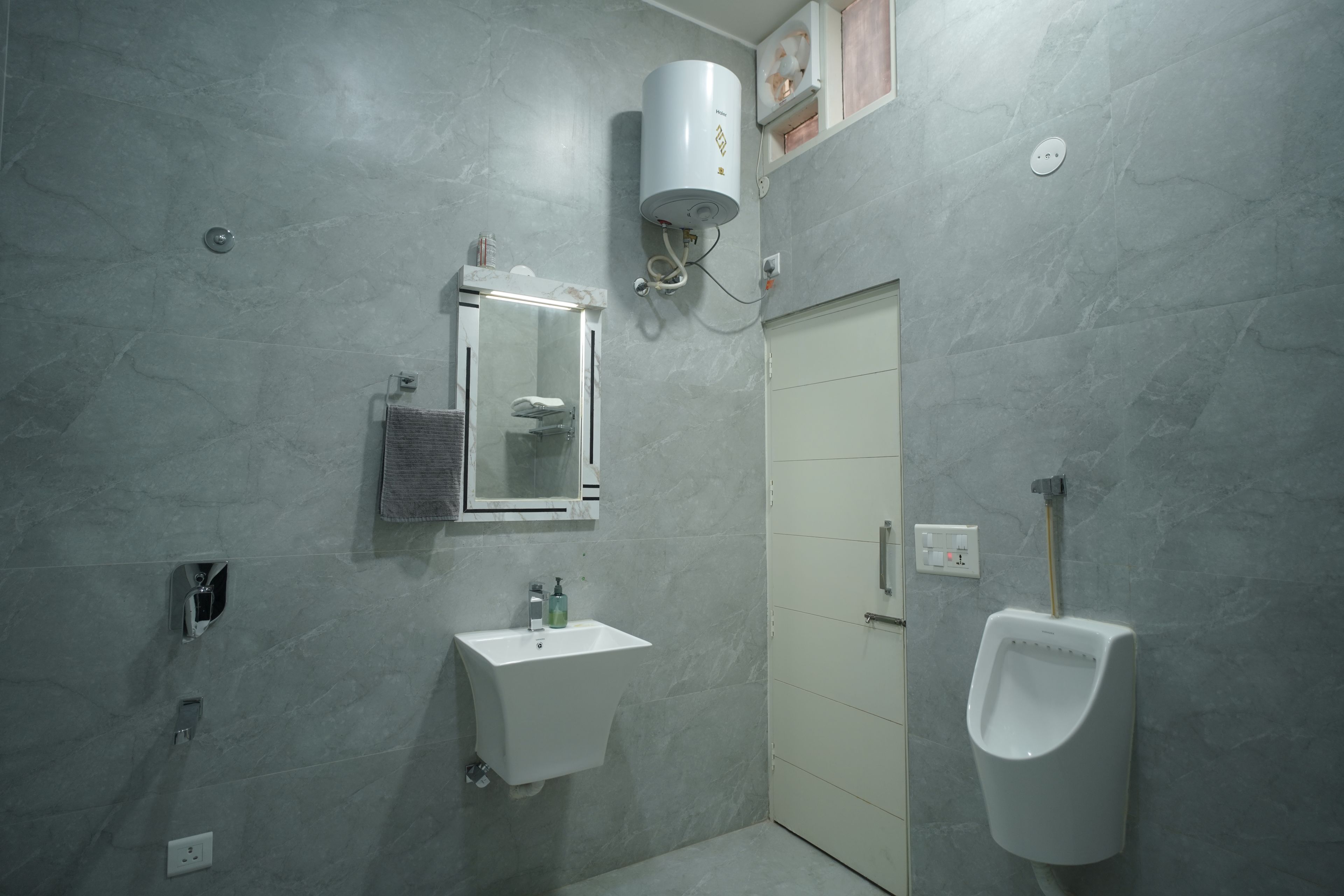 A bathroom with a sink, mirror, towel rack, urinal, and a shower area.