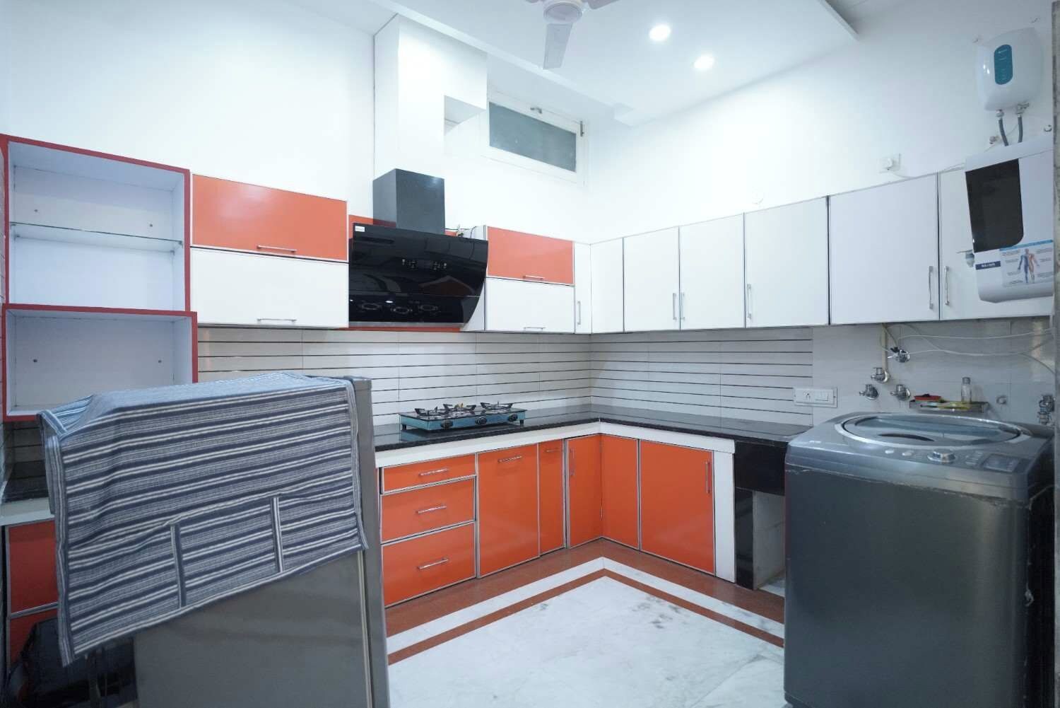 A compact kitchen with modern appliances, white and orange cabinetry, and a tiled backsplash.