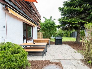 An outdoor patio with a barbecue grill, wooden benches, and a white building with a window. - Quarter 6 Apartment 8 (Büsum)