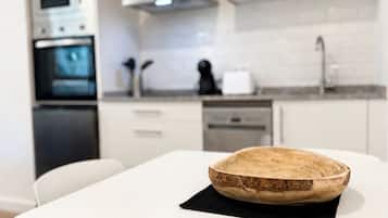 Eine moderne Küche mit weißen Schränken, einer Holzschüssel auf einem Tisch und einem weißen Esszimmerstuhl.