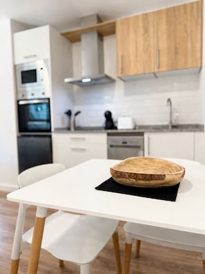 A modern kitchen with white cabinetry, a wooden bowl on a table, and a white dining chair.