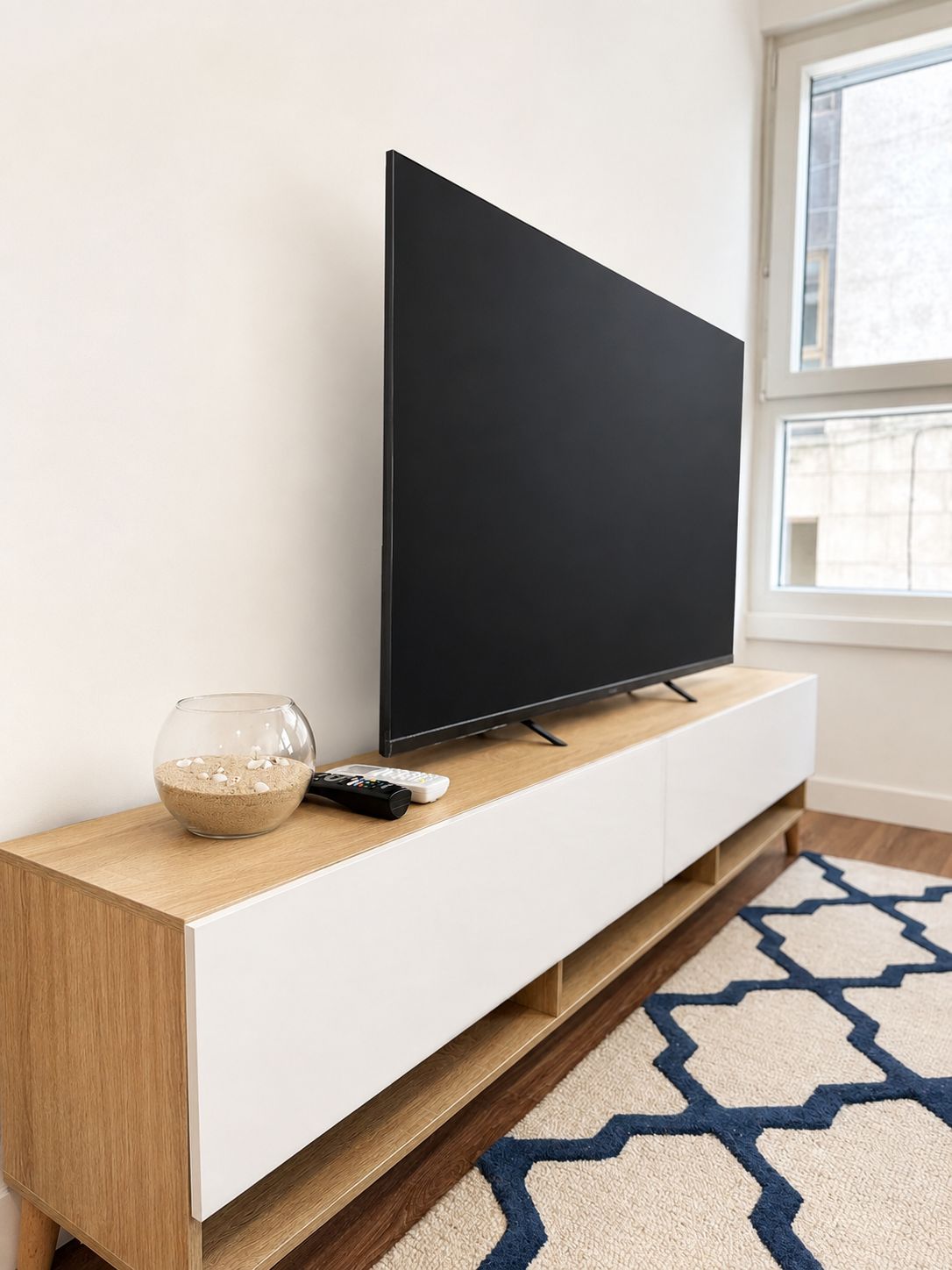 A flat-screen TV on a white TV stand with a remote control and a decorative bowl.