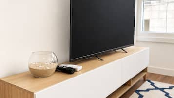 A flat-screen TV on a white TV stand with a remote control and a decorative bowl.