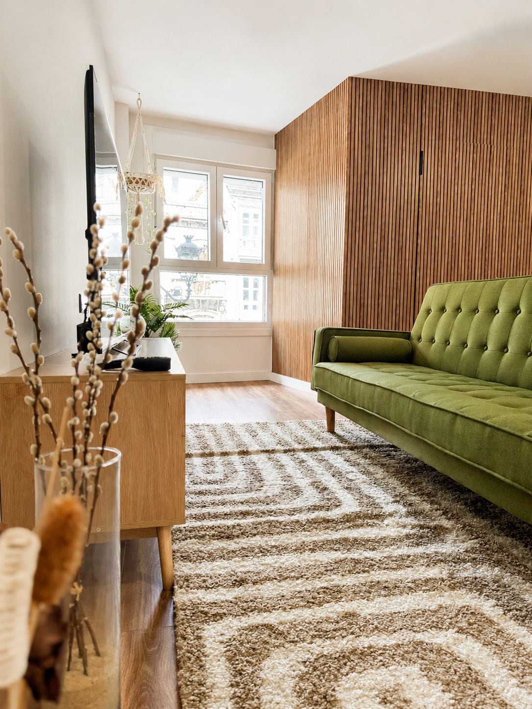 A modern living room with a green sofa, wooden panel wall, and a patterned rug.