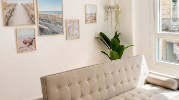 Una sala de estar con un sofá color beige, una planta de macramé colgante y cuadros con motivos playeros en la pared.