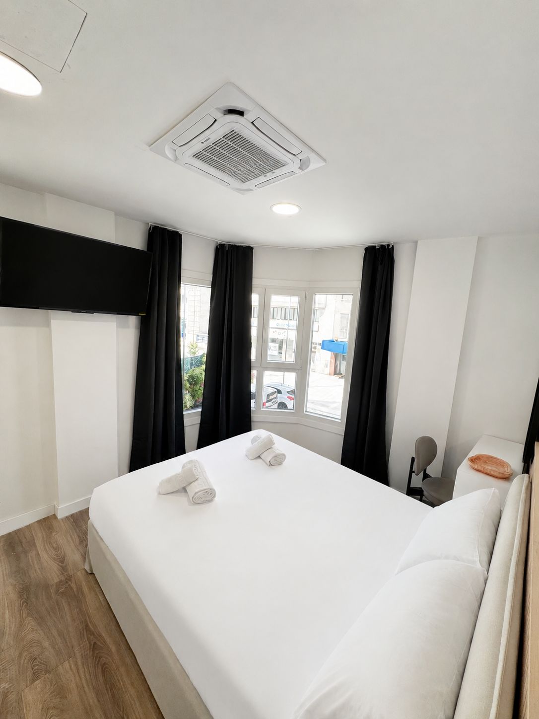 Ein Hotelzimmer mit einem Bett, einem Flachbildfernseher, einem Fenster mit Vorhängen und einem Deckenlüfter.
