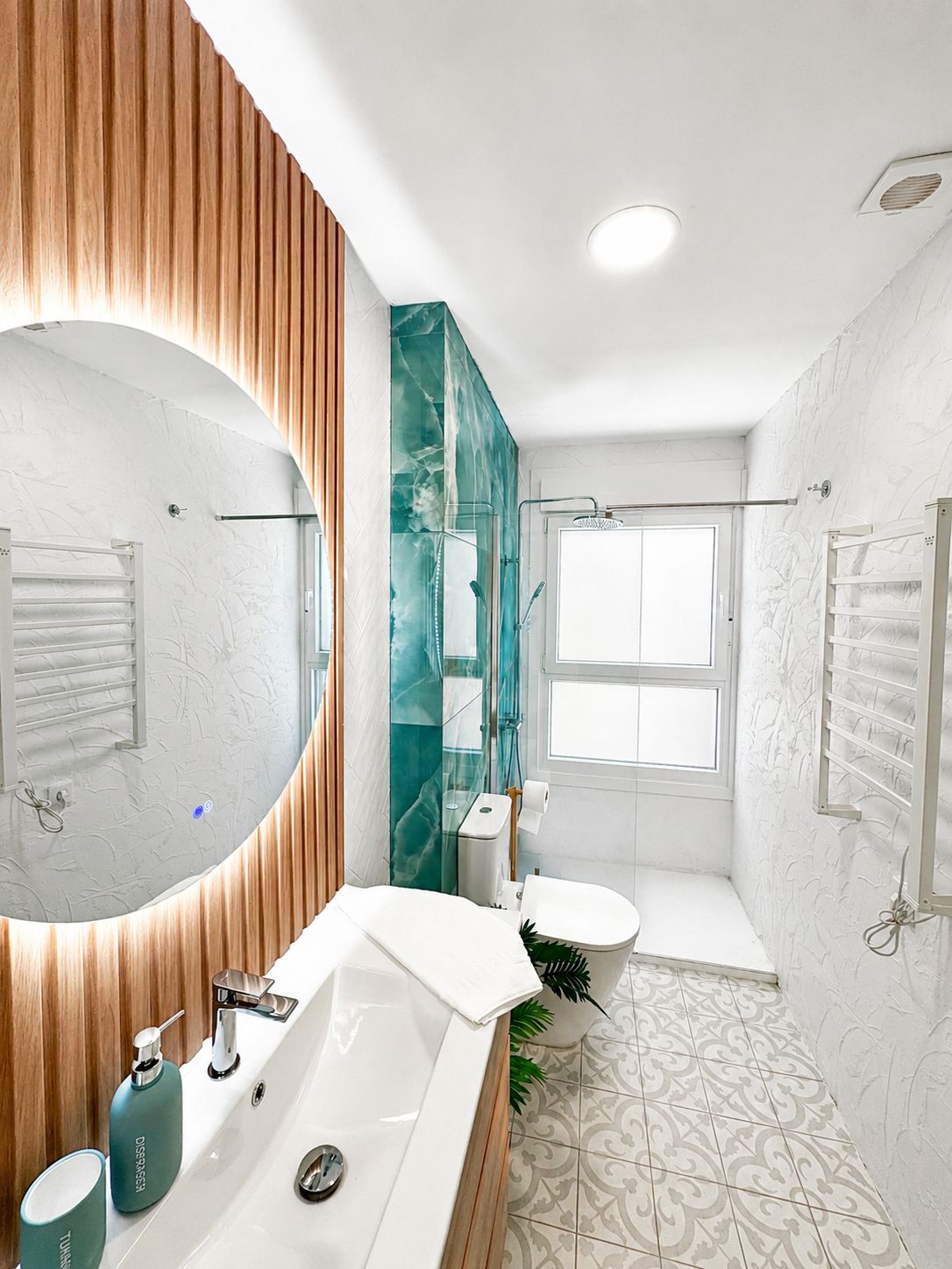 Un baño moderno con un espejo grande, un lavamanos blanco, un inodoro y una zona de ducha.