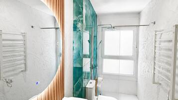 Un baño moderno con un espejo grande, un lavamanos blanco, un inodoro y una zona de ducha.