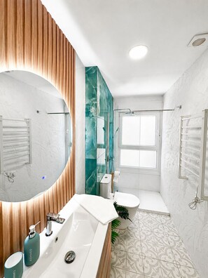 Un baño moderno con un espejo grande, un lavamanos blanco, un inodoro y una zona de ducha.