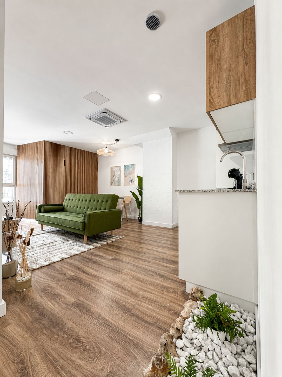Una sala moderna con un sofá verde, suelo de madera y una pared blanca con estantería empotrada.
