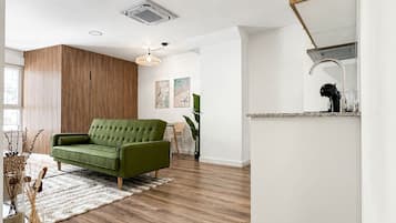 Una sala moderna con un sofá verde, suelo de madera y una pared blanca con estantería empotrada.