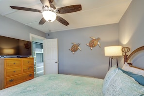 Ein Schlafzimmer mit Bett, Schminktisch, Deckenventilator und Wandbildern.