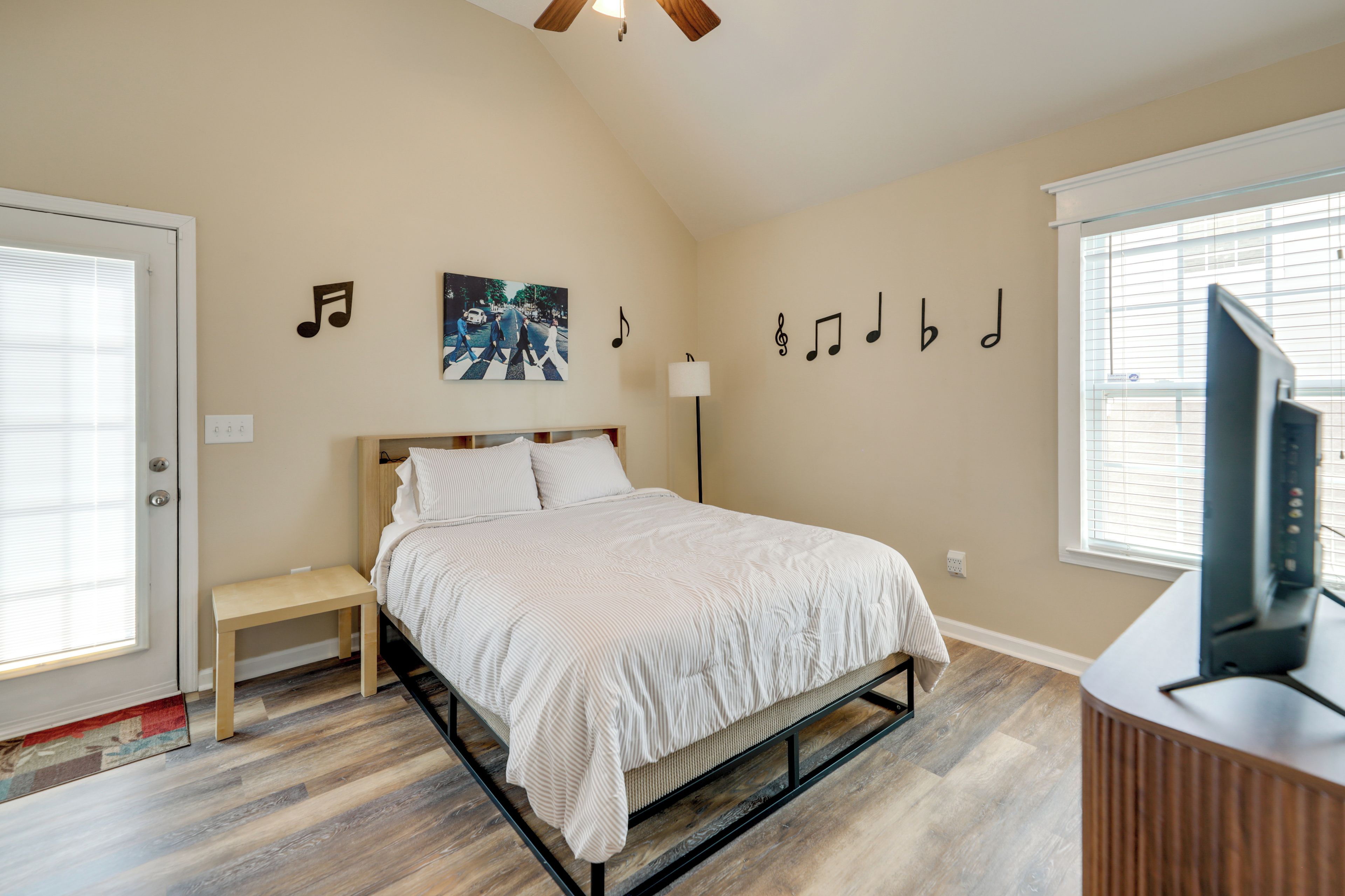 Quarto com cama, mesa de cabeceira, abajur e parede decorada com notas musicais e a capa de um álbum dos Beatles.