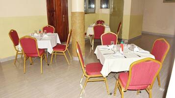 A dining area with tables set for four, each with red upholstered chairs and white tablecloths.