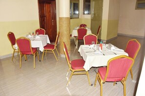 A dining area with tables set for four, each with red upholstered chairs and white tablecloths. - Race Hotel Mbale (Mbale)