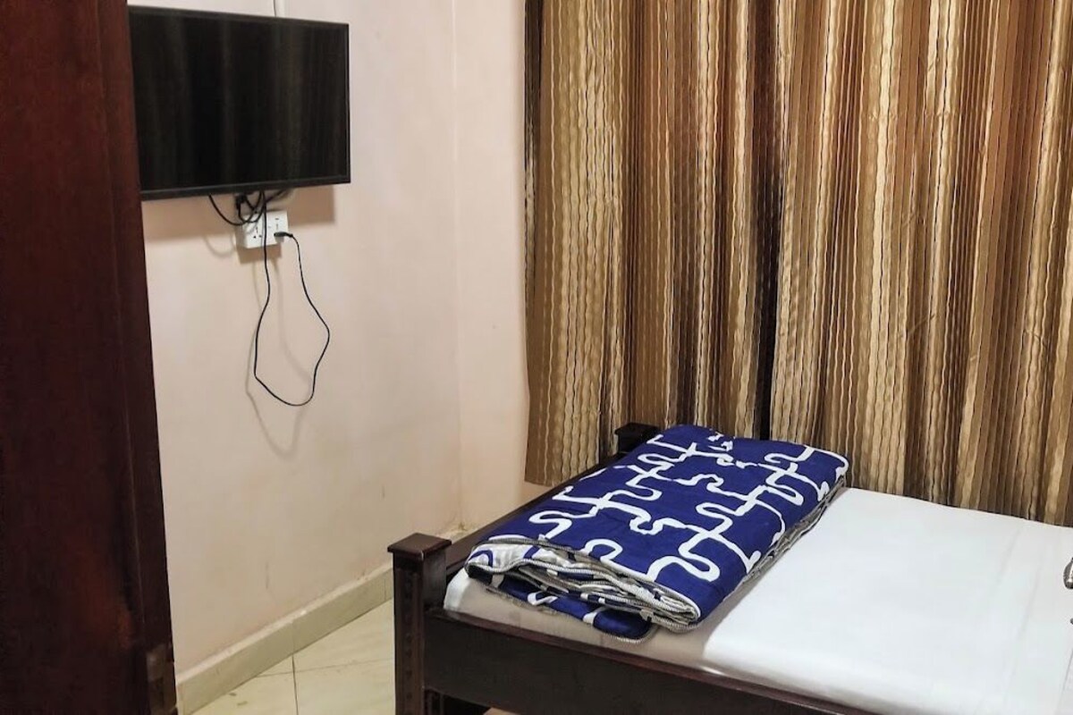 A room with a bed, a flat-screen TV mounted on the wall, and a curtain.