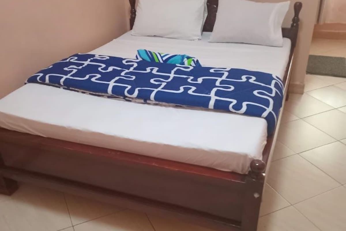 A single bed with a wooden frame, white bedding, and a blue patterned blanket.