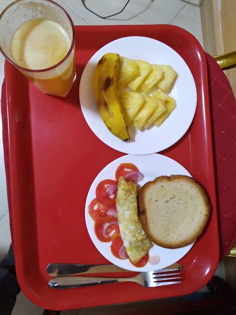 Una safata amb un got de suc, un plat amb rodanxes d'anana, un plat amb truita i tomàquet, i una làmina de pa.