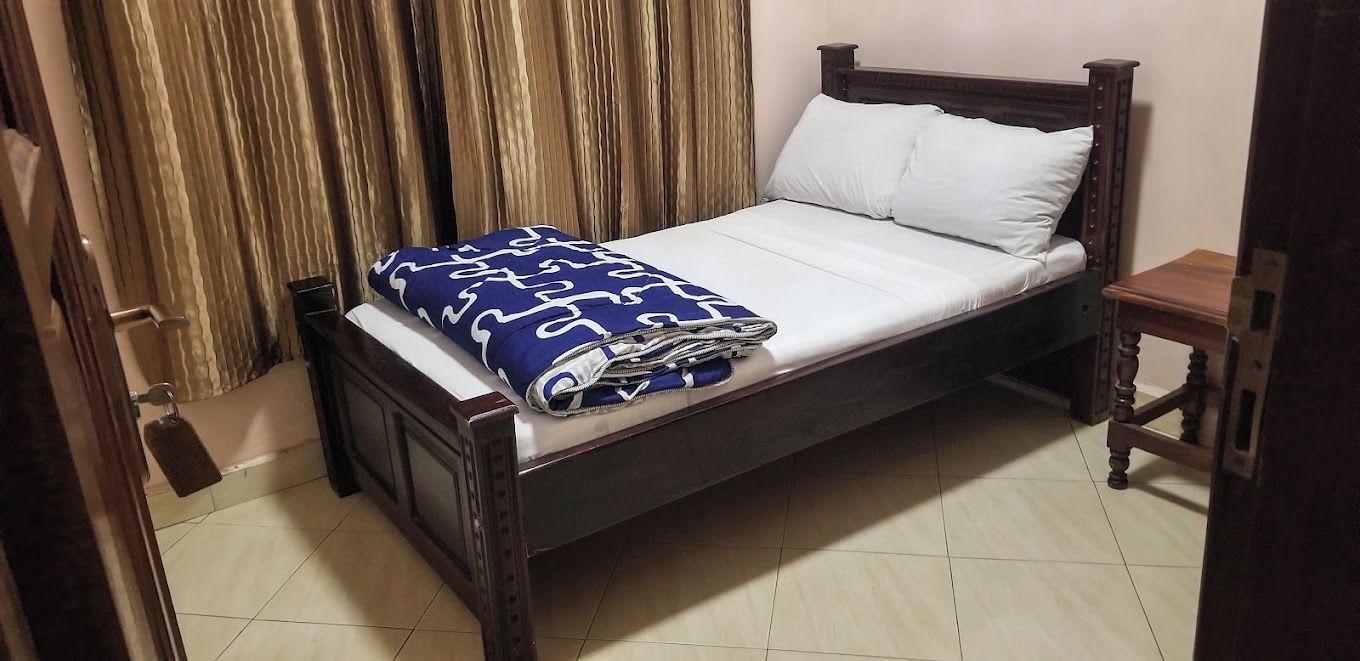 A single bed with a wooden frame, a white mattress, and a blue patterned blanket.