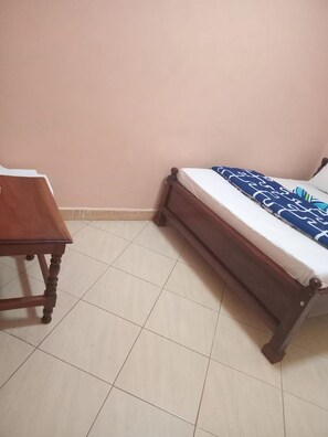 A bedroom with a bed, a wooden table, and a tiled floor. - Race Hotel Mbale (Mbale)