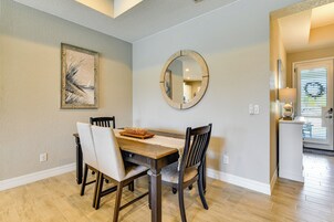 Un comedor con una mesa de madera, cuatro sillas, un espejo redondo y un cuadro en la pared.
