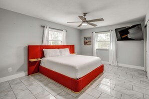 Ein Schlafzimmer mit einem roten Bett, weißer Bettwäsche, einem Deckenventilator und zwei Fenstern mit weißen Vorhängen.
