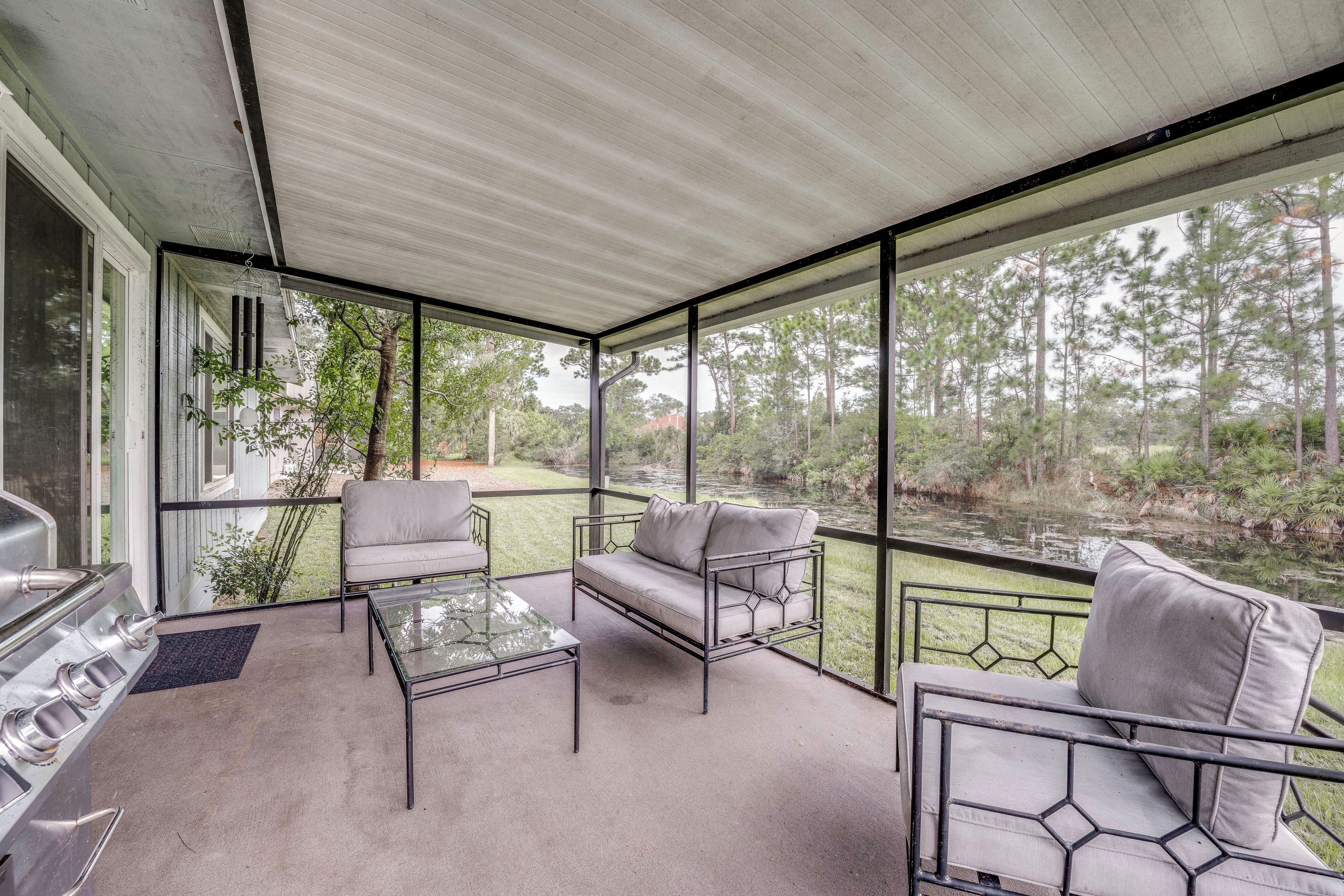 A covered patio with a grill, two sofas, and a glass table.
