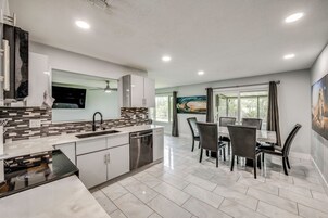A modern kitchen with a dining area, featuring a large island, built-in appliances, and a view through the window.