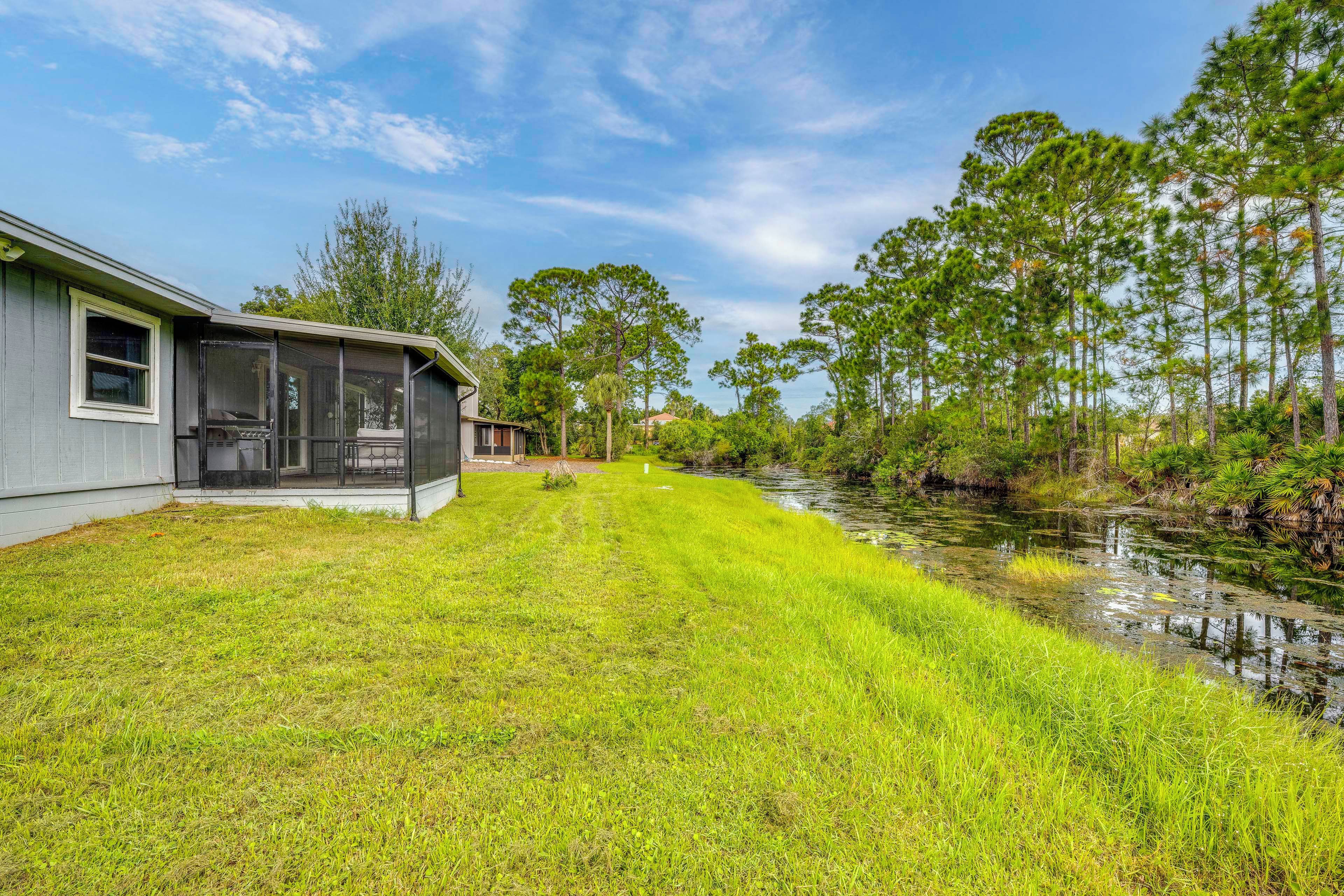 A residential property with a covered outdoor seating area, a grassy lawn, and a body of water.