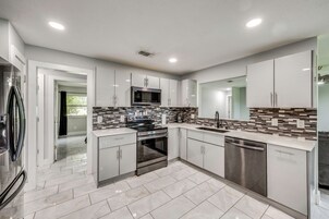 Una cocina moderna con electrodomésticos de acero inoxidable, armarios blancos y salpicadero de azulejos.