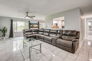 A modern living room with a sectional sofa, a glass coffee table, and a ceiling fan.
