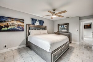 A bedroom with a bed, a ceiling fan, a nightstand, a dresser, and a painting on the wall.