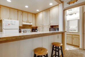 A kitchen with wooden cabinets, a white refrigerator, a stove, and two stools. - Steps to Slopes! Mammoth Mountain Condo (Mammoth Lakes)