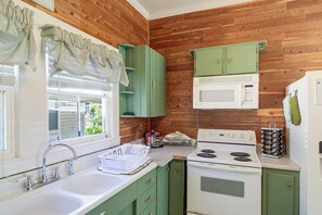 A kitchen with wooden walls, a white stove, a microwave, and green cabinets. - 2 Mi to Dtwn Pensacola: Historic Home w/ Patio! (Pensacola)
