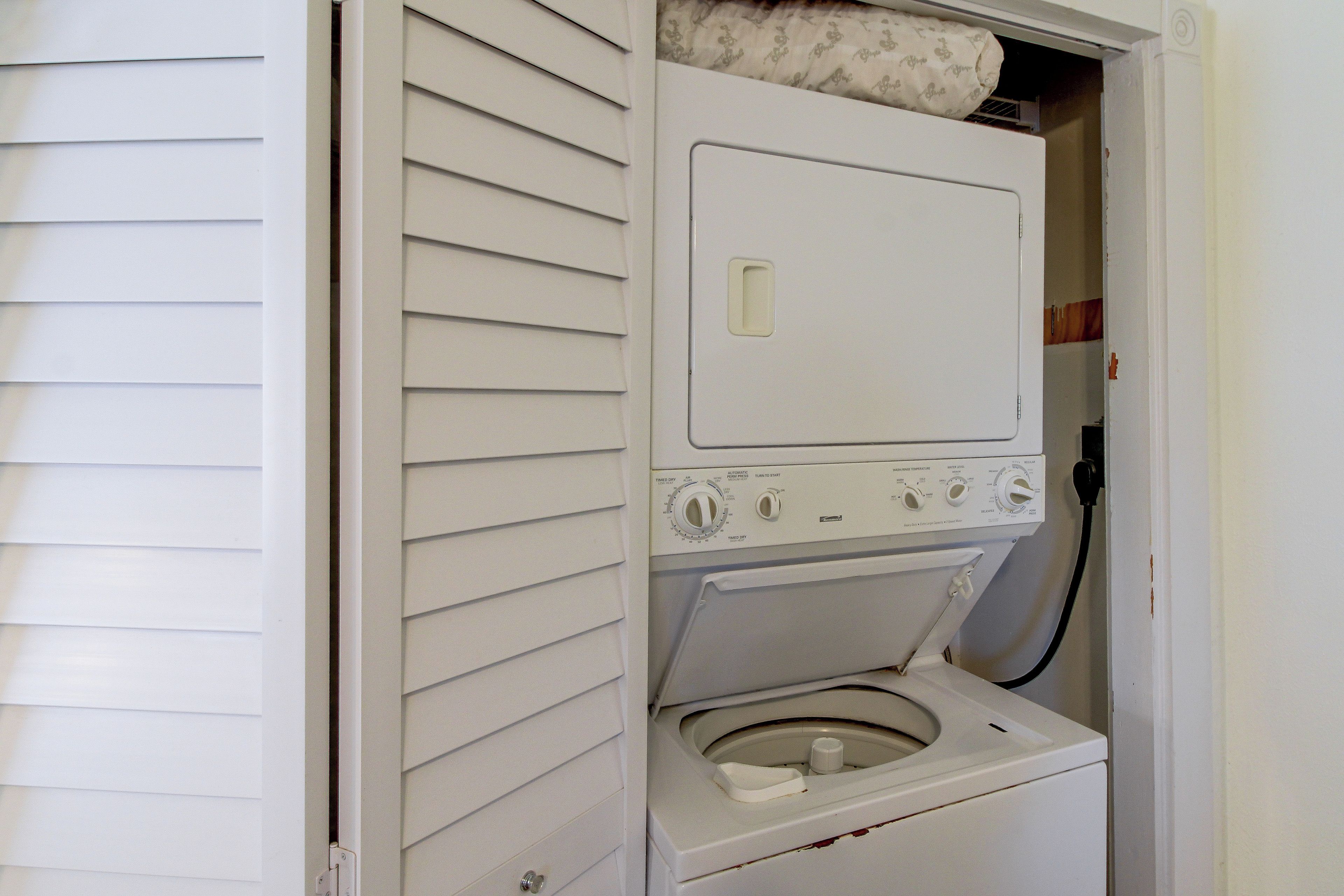 A compact, white, wall-mounted washer and dryer unit with a control panel featuring multiple dials and buttons.